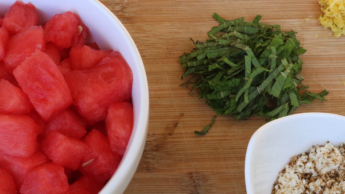 A bowl of cut up watermelon, and a pile of cut up mint on a cutting board. 