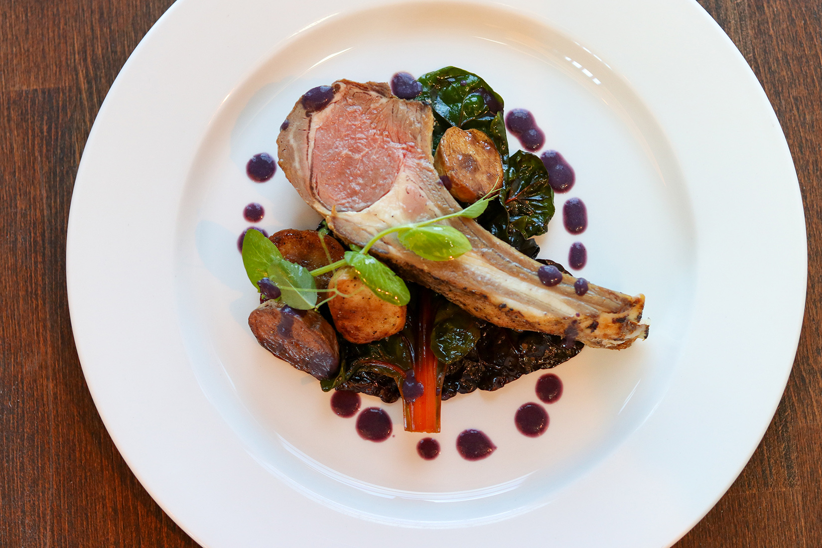 A plated rack of lamb with vegetables and sauce.