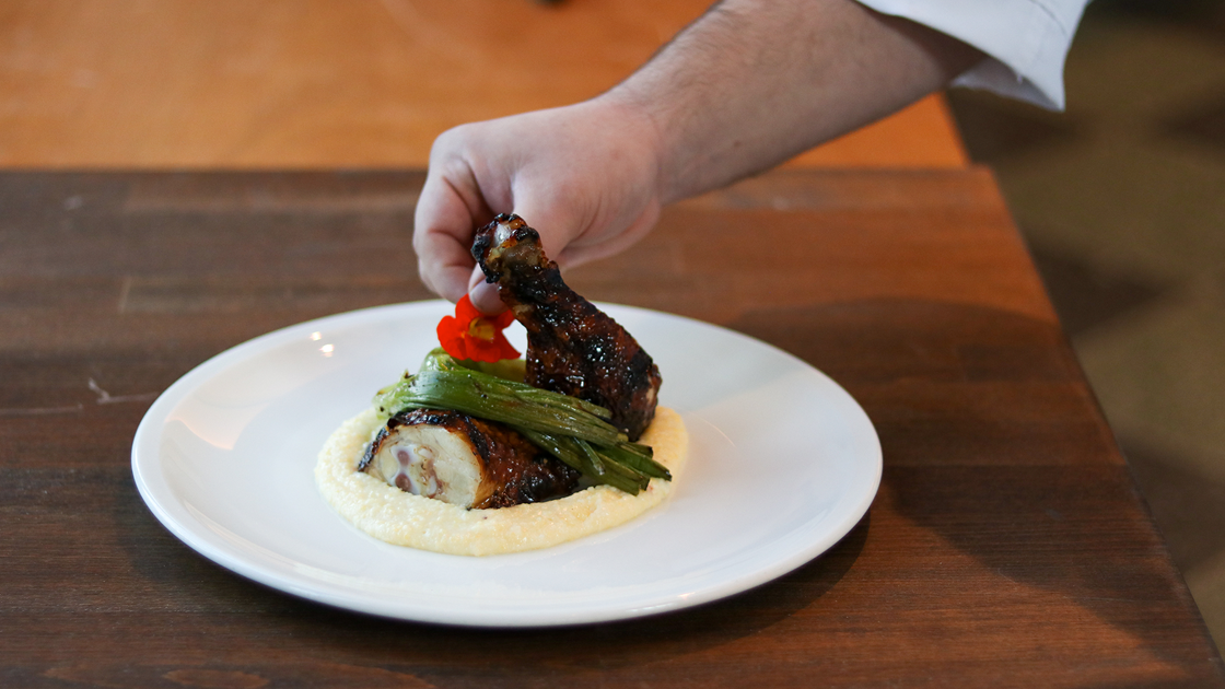 A hand plating a dish of chicken thighs and polenta.