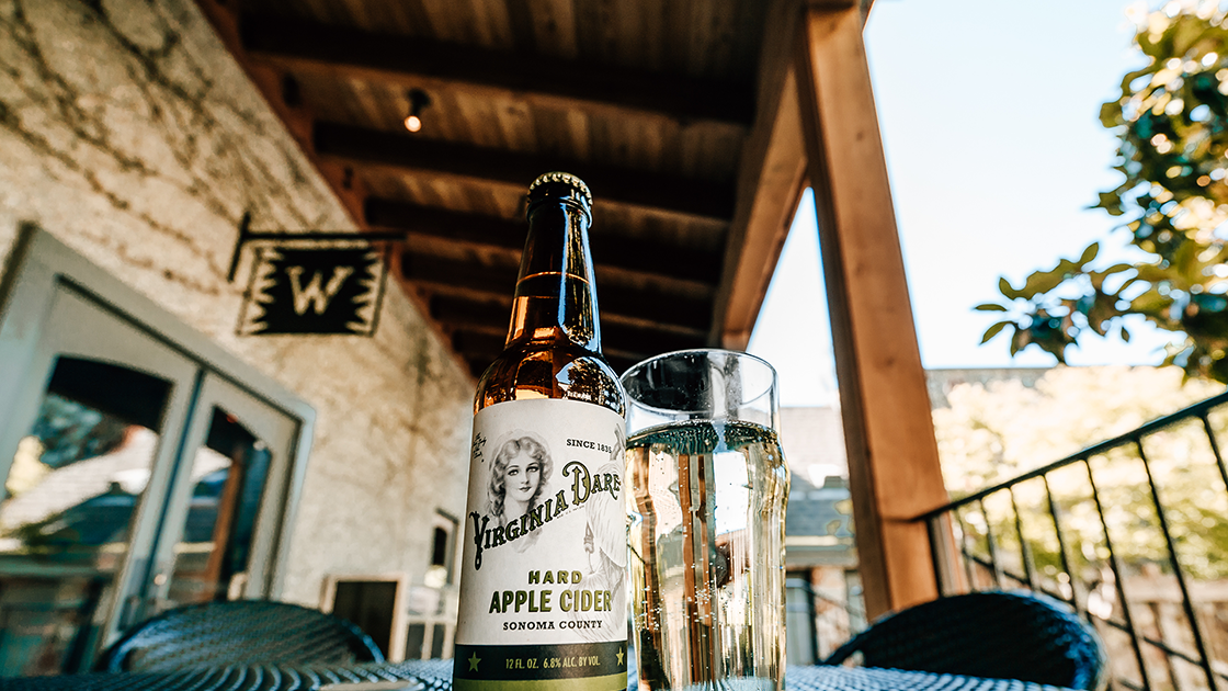 Bottle of Virginia Dare Hard Apple Cider and a glass on a sunny patio.