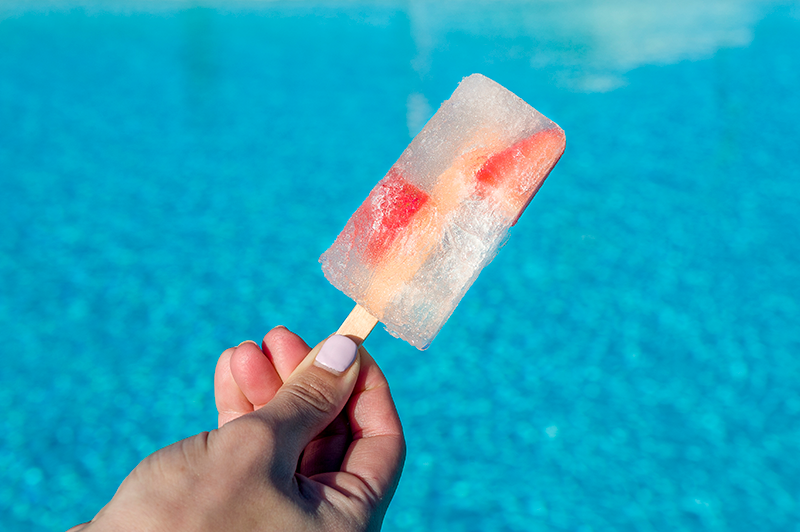 Popsicle held up in front of a pool.