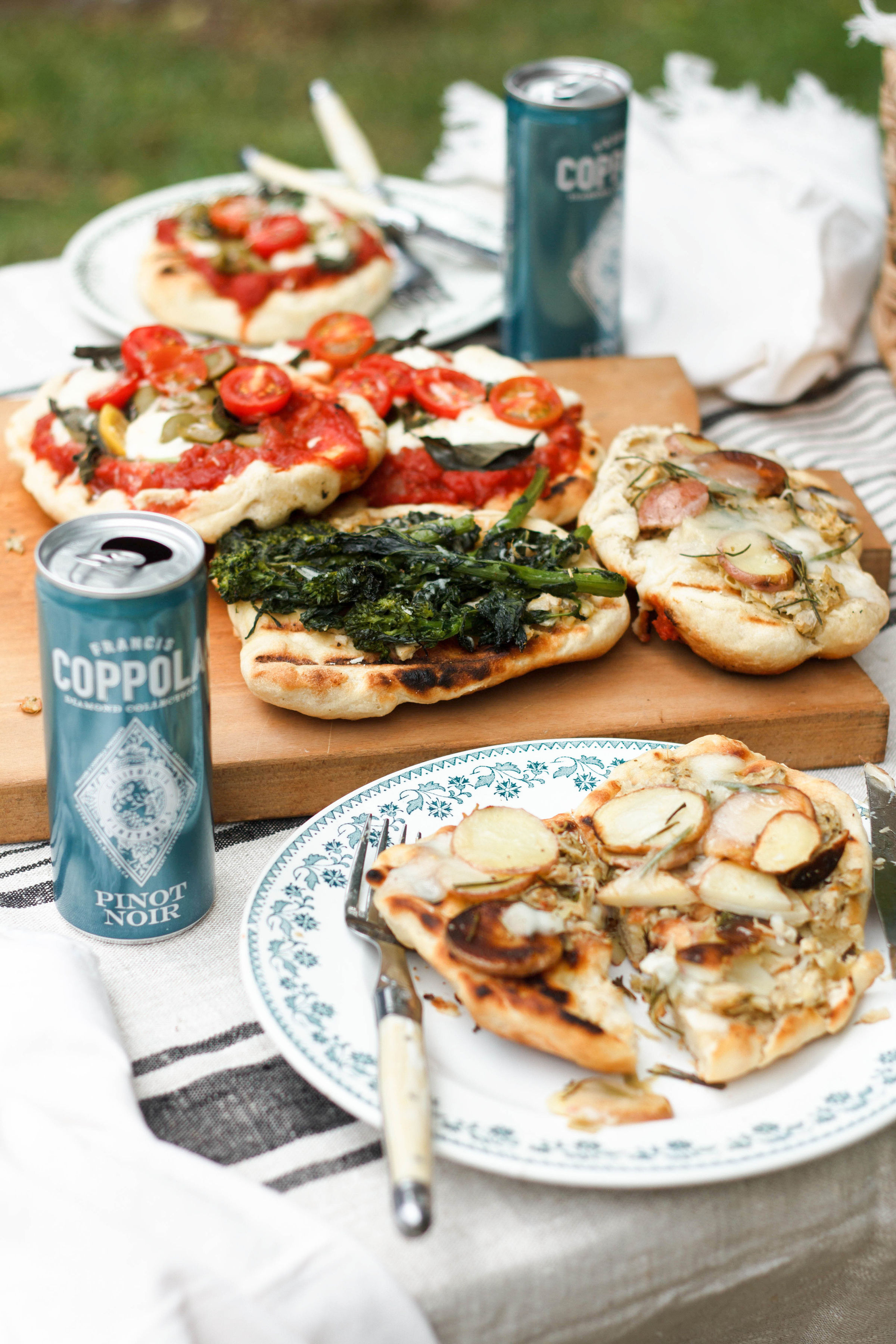 A table with an assortment of grilled pizzas and cans of pinot noir.