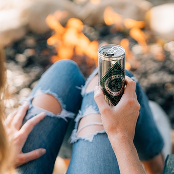 Woman's knees by a campfire holding a can of Diamond Collection wine.