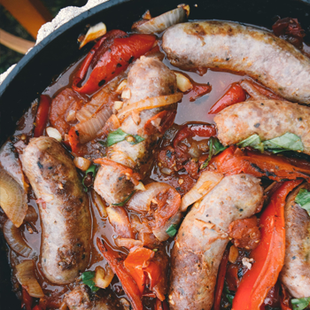 Close up of sausages and red peppers cooking in a cast iron skillet.