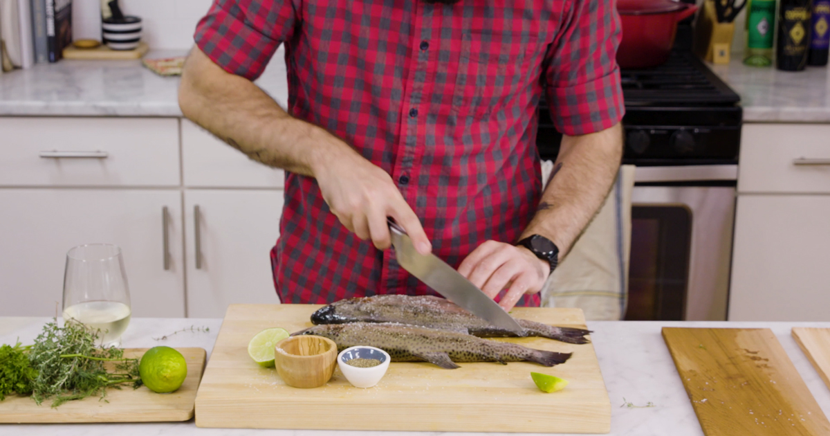 A man using a knife to prepare a trout for cooking.