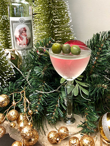 A Countess Walewska vodka bottle nestled about pine tree branches with a Martini in a glass garnished with three olives. 