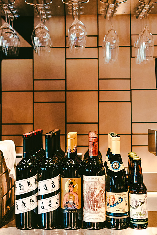Bottles of Director's Cut Zinfandel, Director's Cut Cabernet Sauvignon, Manteo, Lost Colony Red Blend, Virginia Dare Pinot Noir, and Virginia Dare Hard Apple Cider on a tasting bar lined up.