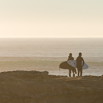 A pair of surfers standing on a cliff over the ocean.