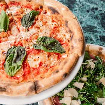 Two pizzas on a green marble table.